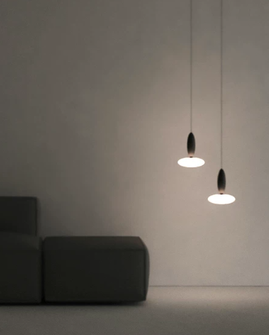 Two modern pendant lights with dark teardrop-shaped shades and glowing oval white shades hanging in a minimalist room next to a dark gray sofa.